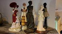 Overall view of seven assorted figurines including a Venus de Milo style statue, a ballerina, and fashion lady figures with some acting as decanters.