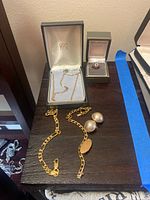 Overview of all jewelry items on wooden surface: necklace in box, bracelet with monogram plate, pearl earrings, ring in box.
