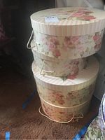 Stacked floral hat boxes with rope handles in a room setting.