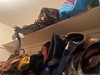 Overview of various purses and bags arranged on shelves including dark brown, black, and colored bags.