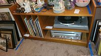 Photo showing wooden stereo cabinet with decorative figurines on top, shelves holding vinyl records, stereo receiver, and record player.