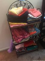 Photo showing stacked vintage clothing items folded and organized on a metal rack including shirts, pants, and tops in various colors and patterns.