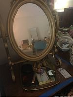 Front view of vintage gold-tone oval vanity mirror with base shelf holding grooming items.