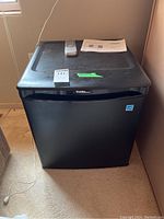 Front view of a black Danby Designer bar fridge with a remote control and instruction manual on top.