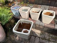 Five ceramic plant pots arranged in two rows on an outdoor brick surface, four smaller pots on the top row and one larger pot below. All pots show glazed interiors with brownish discoloration and some glaze drips. One small pot is cracked.