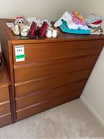 Front view of wood dresser showing five horizontal drawers and items on top including baby shoes, clothes, and stuffed animal
