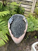 Top angle showing textured black basin surface with water running from center and weathered composite base with damaged edges.