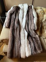 Full-length view of the fur coat laid on a couch, showing two tones of fur: mostly brown with a vertical central stripe of white fur.