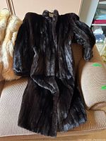 Full view of the dark brown full-length fur coat displayed on a chair showing the fur texture and length.