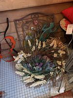 Photo showing large floral wreath with white and purple flowers, brown twig base, and metal garden wall art including a green gecko and bird decoration.