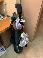 Golf bag with clubs inside, including multiple club headcovers and attached golf shoes and visors.