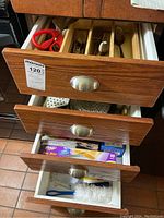 Three drawers partially opened showing kitchen wrap foil in one drawer, a masher and whisk in the other, and kitchen utensils in the top drawer.