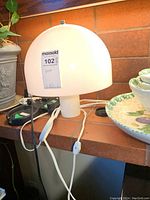 Front view of lamp placed on shelf with plant and dish nearby