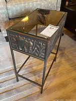 Full view of the rectangular metal side table with glass top, showing embossed pattern on side panels.