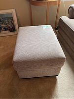 Front left angle view of the ottoman showing upholstery texture and overall shape.