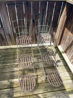 Two metal plant stands with three circular pot holders each, showing rust and weathering.