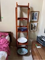 Full view of wooden ladder-style shelf with 4 shelves, next to bed and dresser, holding decorative bowls (contents not included).