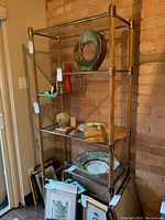 Full front view of six-tier wood, metal and glass shelf against brick wall with decorative items on shelves.