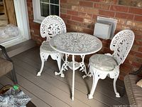 Front view of white painted cast aluminum bistro table and two matching chairs on deck