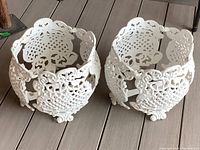 Two white cast aluminum planters with floral and lattice cutout designs, viewed slightly from above, placed on wooden floor.