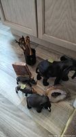 Lot arranged on floor showing carved wood elephants, wood utensils with animal tops, marble geode, and petrified wood slice.