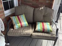 Front view of steel two-seater bench with beige cushions and two striped throw pillows showing condition and details.