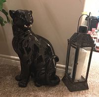 Front view showing ceramic jaguar sculpture seated next to steel lantern with pillar candle