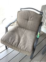 Steel patio chair with beige cushions taken close up from left side angle.