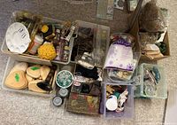 Wide overhead view of multiple containers grouped together each holding assorted craft items including paints, miniatures, flower arranging materials, glass marbles, and wood plaques.