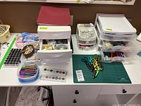 Craft supplies including storage drawers, scissors, markers, cutting mats, and crafting containers arranged on table