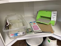 Full lot including Cuttlebug machine, storage bin with dies and accessories placed on a corner shelf.