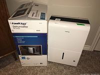 Photo of KoolKing dehumidifier next to its original packaging box, showing overall size and branding on box.