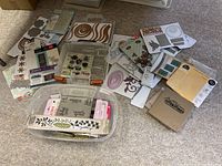 Wide view of overall collection spread on carpeted floor shows several packages of die cuts and stencils along with clear containers with stamps.