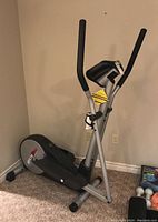 Full view of the elliptical crosstrainer standing on carpet, showing the frame, handlebars, foot pedals, and the branding on the lower side area.