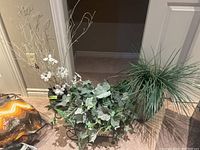 Faux plants in ceramic and metal planters displayed on the floor with beige walls in the background.
