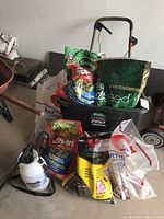 Full view of Scotts Turf Builder Pro seed spreader with multiple bags of lawn seed, fertilizer, and insect killer arranged in front, along with the pump sprayer on the concrete floor.