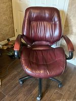 Front view of the burgundy leather office chair showing padded seat, backrest, and wooden padded armrests.