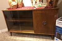 Front view of the mid-century modern wooden buffet with sliding glass doors on the left and single door with decorative metal handle on the right, topped with a red fabric runner.