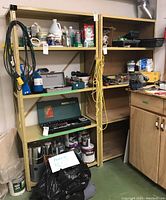 Two steel utility shelving units with wooden shelves holding workshop tools and supplies, not included in sale.