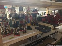 Nutcracker group arranged on a wooden shelf including big king nutcracker, traditional soldier, smaller models, along with large black wall letter and fake florals on the right.