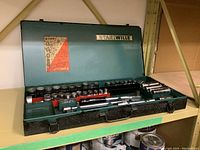 Opened metal blue-green textured carrying case with various sockets, extensions, and attachments inside, arranged in specific slots.