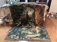 Photo of large tapestry featuring a peacock in a garden setting, partially draped over a sofa, showing detailed woven design and colors.