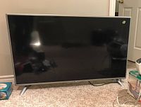 Front view of LG 50-inch LED TV with black screen and silver frame standing on carpeted floor.