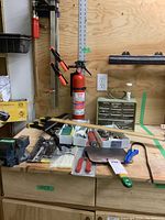 Overall lot view showing clamps, fire extinguisher, parts storage container on bench, hand tools scattered on bench surface