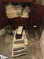 Photo showing folded beige and off-white towels, black metal toilet roll racks, and bathroom mats on floor.