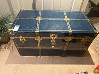 Front view of blue metal trunk showing brass locks, handles and scratches from use.
