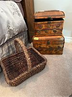 Photo showing both wooden veneer chests stacked and the dark brown woven wicker basket in front on carpeted floor near bed.