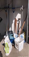 Front view of snow shovels, garden spades, bucket, bags of limestone and ice melt with some tools behind