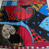 Full view of the scarf showing the colorful abstract pattern with red, black, turquoise, blue, white, and gold colors and various geometric shapes including swirls and checkerboards.