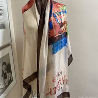 Silk scarf draped over mannequin showing cream base with multicolor abstract pattern and dark brown border